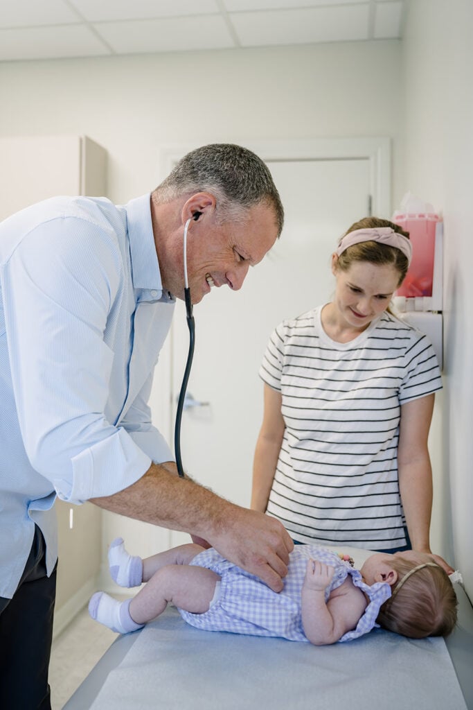 A Here We Grow pediatrician examining a newborn while a parent looks on